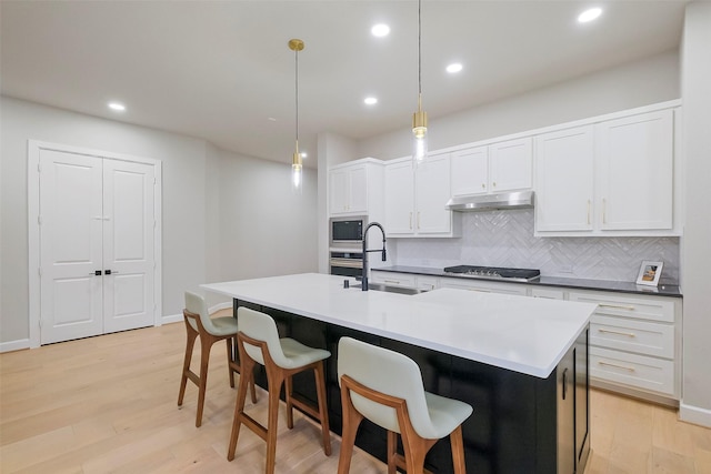 kitchen featuring stainless steel appliances, a sink, light wood-style flooring, and under cabinet range hood