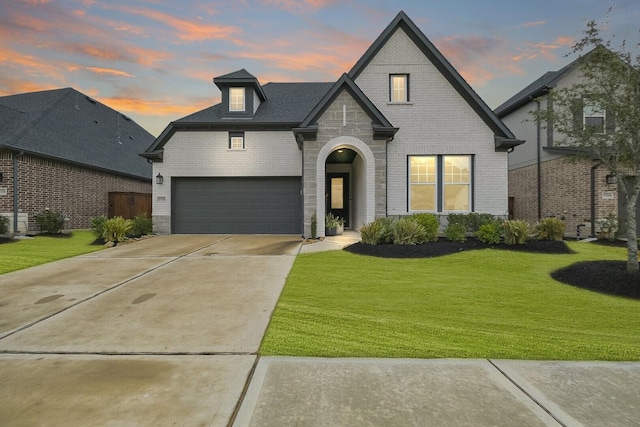 french country style house with a garage, a yard, brick siding, and concrete driveway