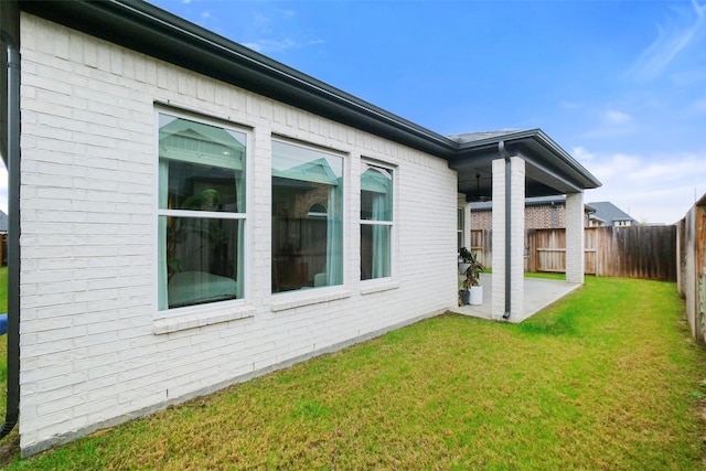 view of side of property featuring a fenced backyard, a patio, a lawn, and brick siding