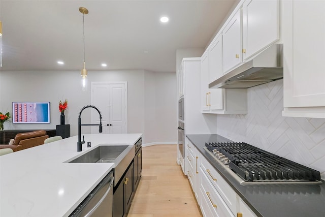 kitchen featuring light wood-style flooring, appliances with stainless steel finishes, white cabinets, a sink, and under cabinet range hood