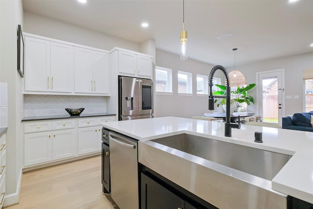 kitchen with a sink, white cabinets, appliances with stainless steel finishes, light wood-type flooring, and decorative light fixtures