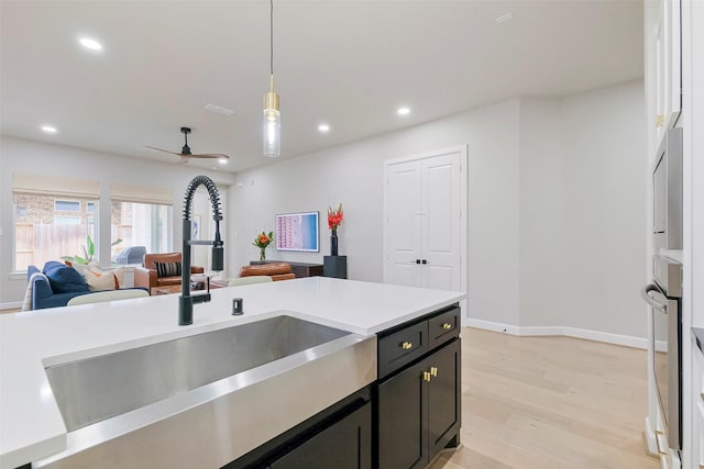 kitchen with recessed lighting, a sink, open floor plan, hanging light fixtures, and light wood-type flooring