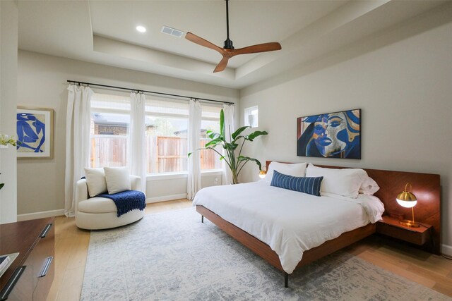 bedroom with light wood finished floors, baseboards, and a tray ceiling