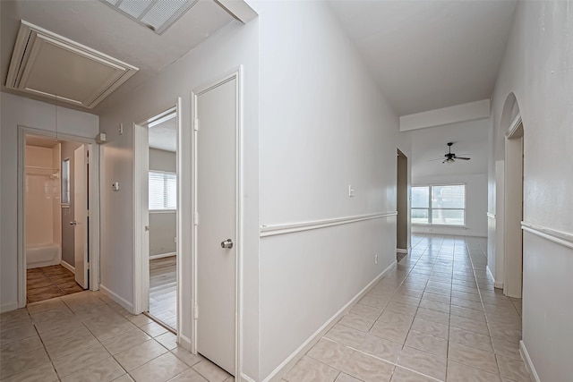 hall featuring a healthy amount of sunlight, light tile patterned floors, attic access, and baseboards