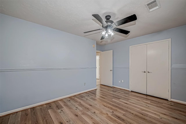 unfurnished bedroom featuring baseboards, visible vents, a ceiling fan, wood finished floors, and a closet