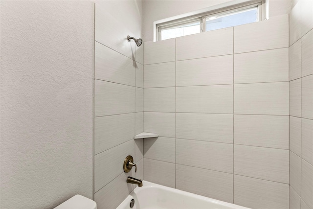 full bathroom with a textured wall, shower / bath combination, and toilet