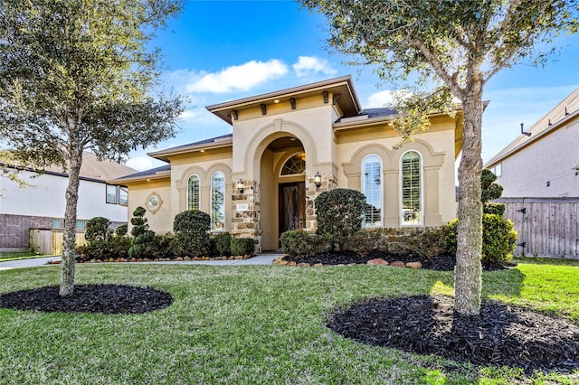 mediterranean / spanish-style home featuring fence, a front lawn, and stucco siding