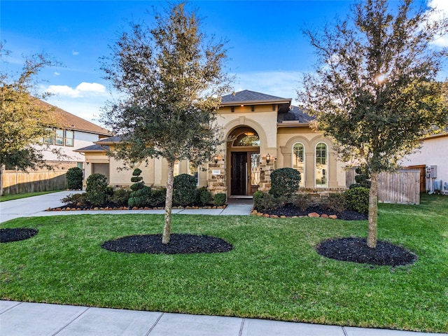 mediterranean / spanish house with a garage, concrete driveway, fence, a front lawn, and stucco siding