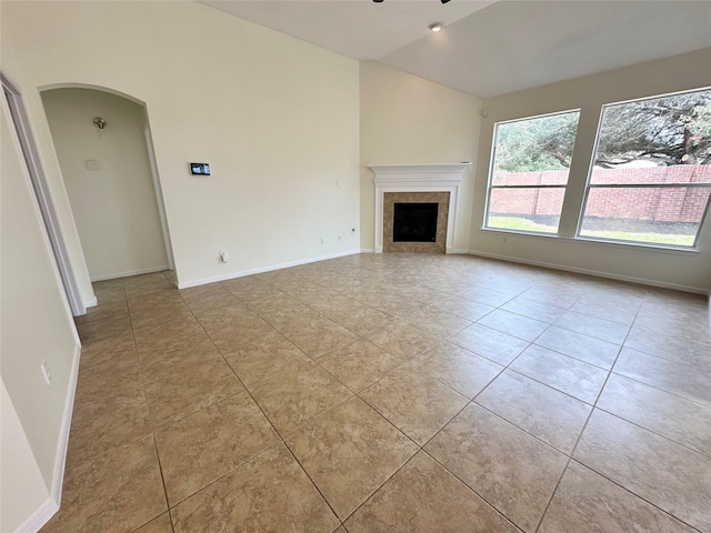 unfurnished living room with arched walkways, lofted ceiling, and baseboards