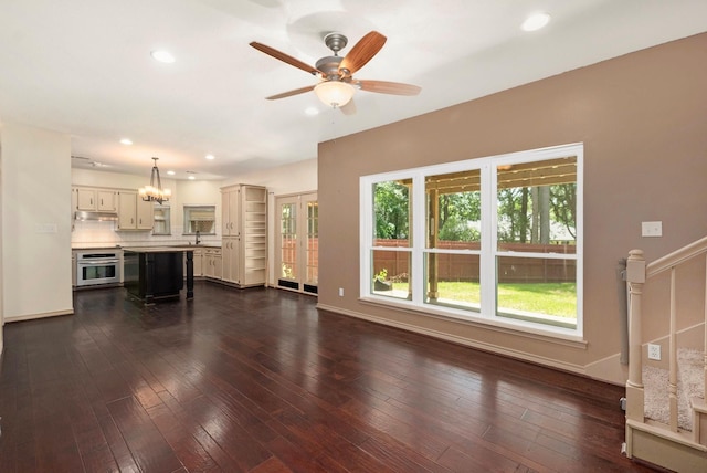 unfurnished living room featuring dark wood-style floors, ceiling fan with notable chandelier, baseboards, and recessed lighting