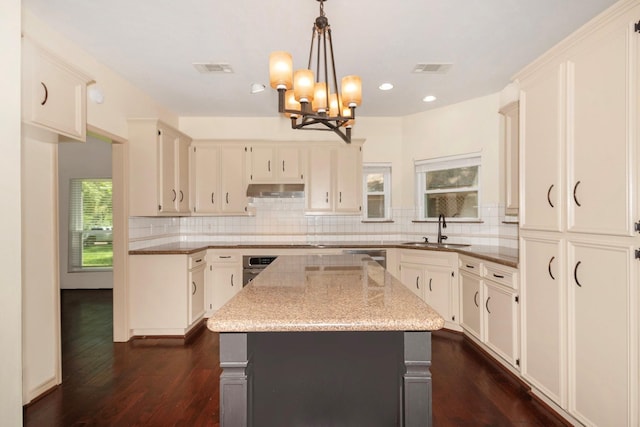 kitchen featuring oven, a sink, backsplash, light stone countertops, and dark wood-style floors