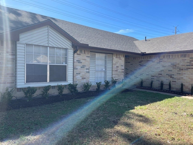 view of side of property with a yard, brick siding, and roof with shingles