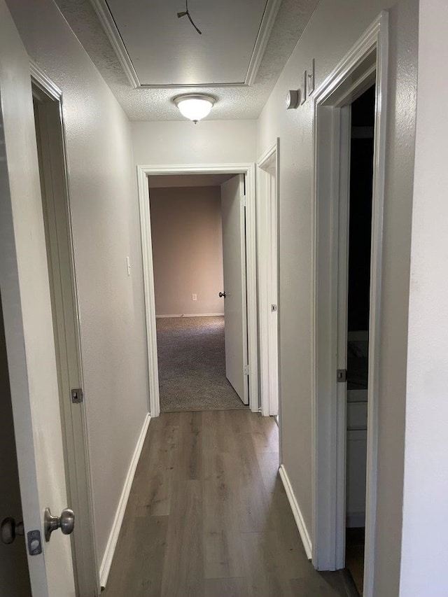 corridor with attic access, dark wood-style flooring, a textured ceiling, and baseboards