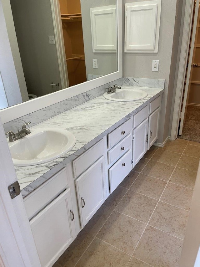 full bath with double vanity, a sink, a spacious closet, and tile patterned floors