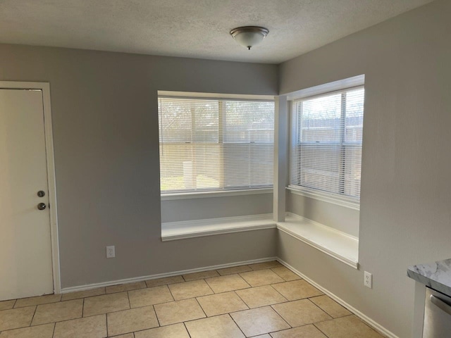 unfurnished dining area featuring baseboards, a textured ceiling, and light tile patterned flooring