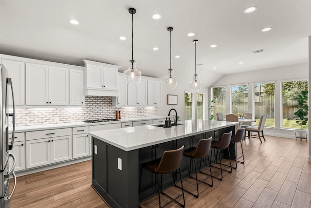 kitchen with visible vents, white gas stovetop, white cabinets, stainless steel fridge, and a sink