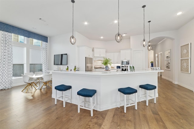 kitchen featuring arched walkways, wood finished floors, white cabinets, appliances with stainless steel finishes, and decorative backsplash