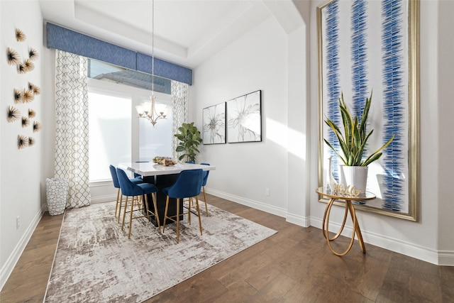 dining space featuring dark wood-style floors, a tray ceiling, a chandelier, and baseboards