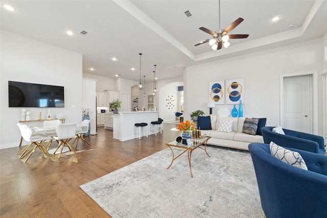 living room with visible vents, a tray ceiling, wood finished floors, and recessed lighting