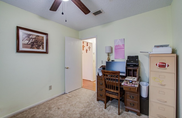 carpeted office with baseboards, a textured ceiling, visible vents, and a ceiling fan