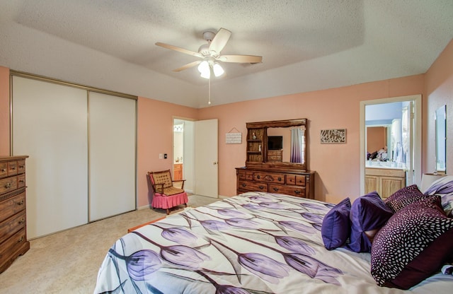 bedroom with a closet, light colored carpet, a textured ceiling, and ensuite bath