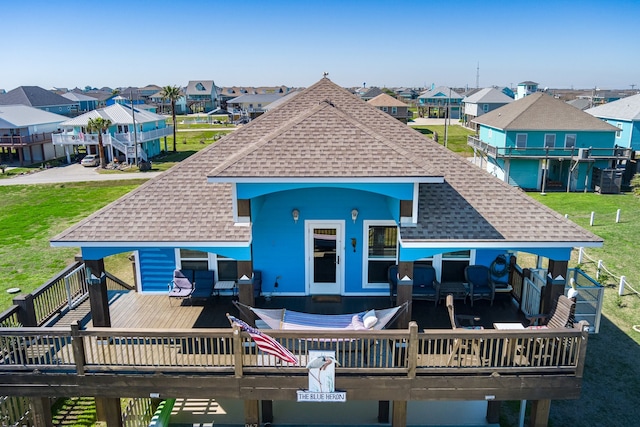 back of house featuring a deck, a yard, roof with shingles, and a residential view