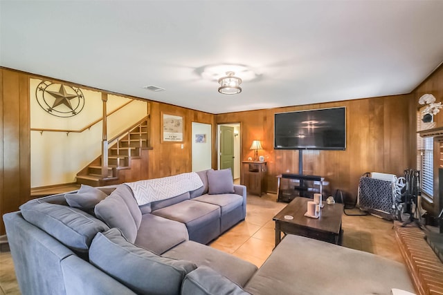 living area featuring light tile patterned floors, visible vents, wood walls, and stairs