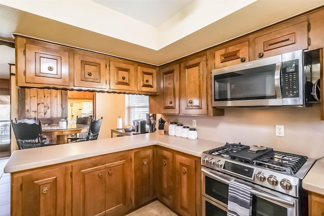 kitchen with light tile patterned floors, brown cabinetry, a peninsula, stainless steel appliances, and light countertops