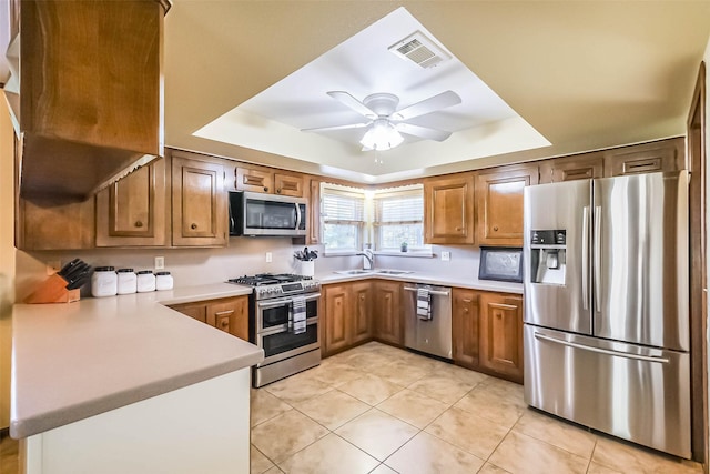 kitchen featuring visible vents, brown cabinetry, a tray ceiling, stainless steel appliances, and light countertops