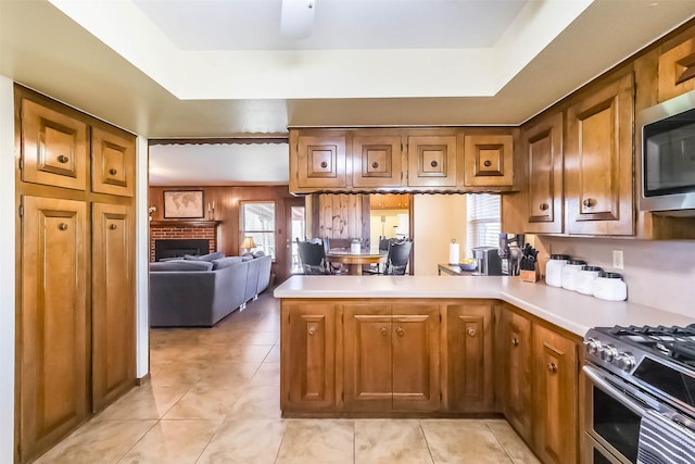 kitchen with a peninsula, stainless steel appliances, a fireplace, light countertops, and brown cabinetry