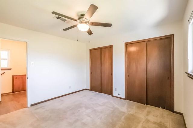 unfurnished bedroom featuring carpet, visible vents, baseboards, and two closets