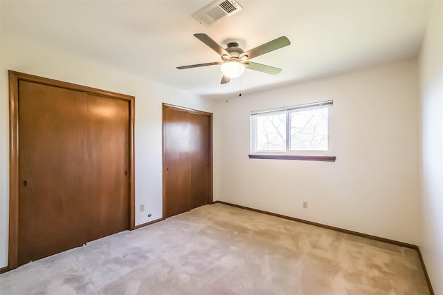 unfurnished bedroom with light colored carpet, a ceiling fan, baseboards, visible vents, and multiple closets