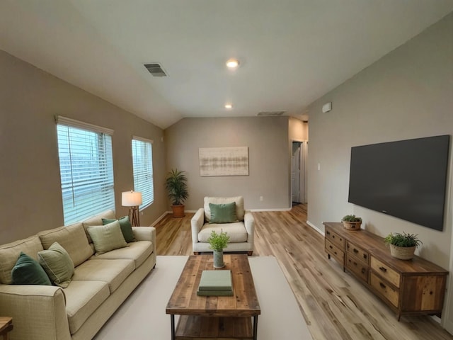 living area featuring light wood-style floors, baseboards, visible vents, and vaulted ceiling