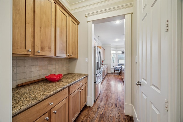 kitchen featuring dark wood-style floors, tasteful backsplash, ornamental molding, dark stone counters, and stainless steel fridge