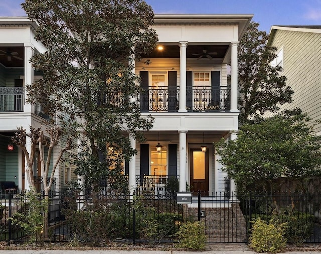 greek revival inspired property with a balcony, covered porch, a fenced front yard, and ceiling fan