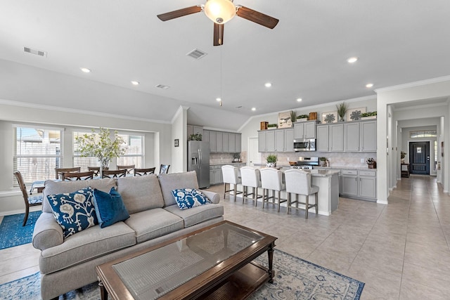 living room with light tile patterned floors, lofted ceiling, visible vents, and crown molding