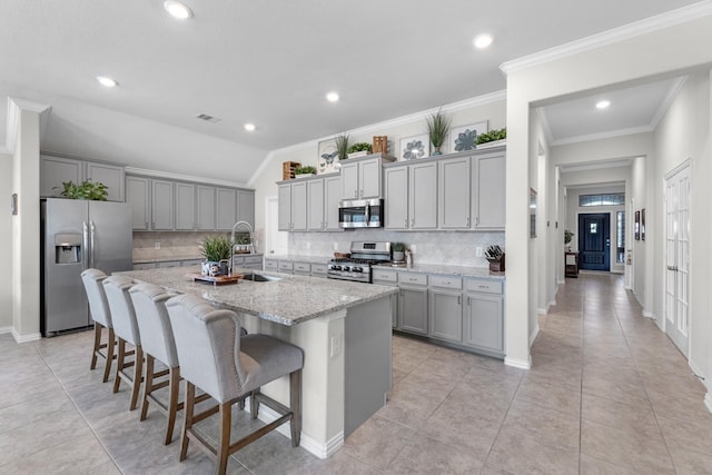 kitchen with a breakfast bar, a center island with sink, stainless steel appliances, gray cabinetry, and a sink