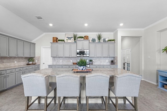 kitchen with a breakfast bar, stainless steel microwave, a kitchen island with sink, and gray cabinetry