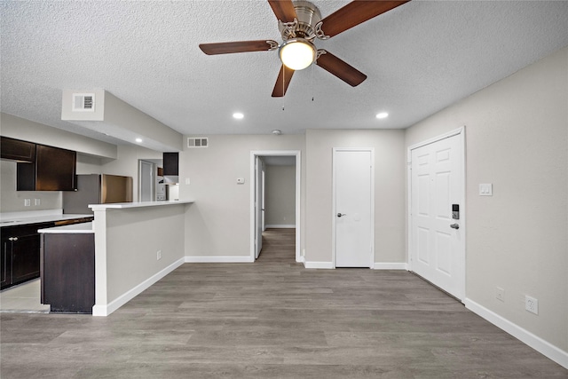 unfurnished living room featuring baseboards, light wood-style flooring, visible vents, and a textured ceiling