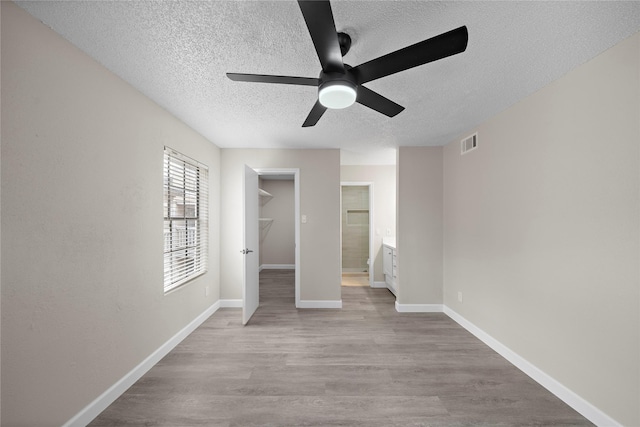 unfurnished bedroom featuring a textured ceiling, wood finished floors, visible vents, baseboards, and a walk in closet