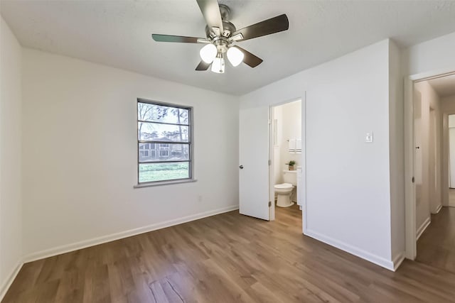 unfurnished bedroom featuring ceiling fan, connected bathroom, baseboards, and wood finished floors