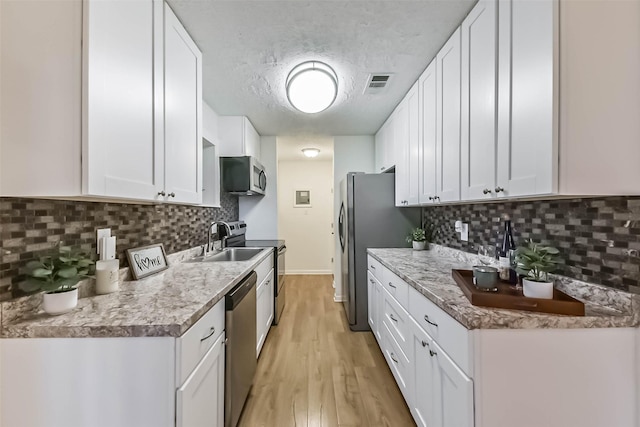 kitchen featuring visible vents, appliances with stainless steel finishes, light wood-style floors, white cabinetry, and a sink