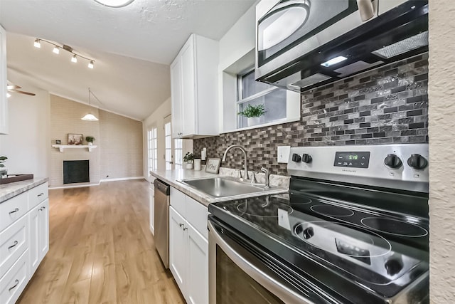 kitchen with a fireplace with raised hearth, appliances with stainless steel finishes, white cabinetry, vaulted ceiling, and a sink