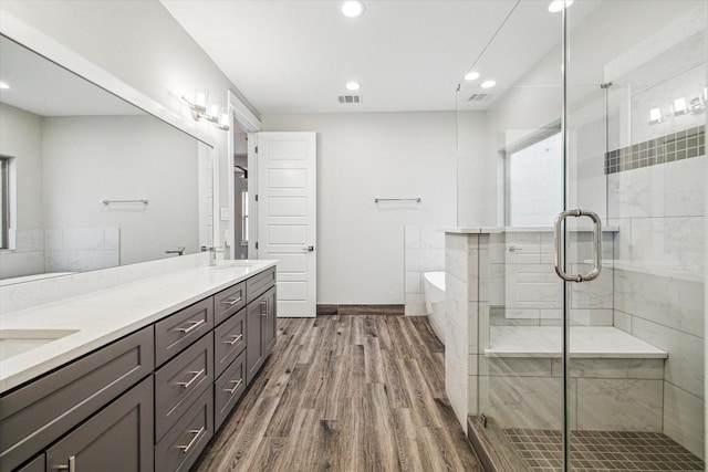 bathroom featuring double vanity, a soaking tub, wood finished floors, a shower stall, and a sink