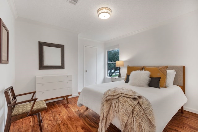 bedroom with baseboards, a textured ceiling, ornamental molding, and wood finished floors