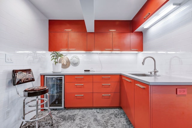 kitchen with tasteful backsplash, red cabinets, wine cooler, light countertops, and a sink