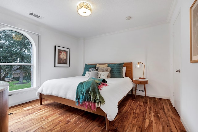 bedroom with baseboards, wood finished floors, visible vents, and crown molding