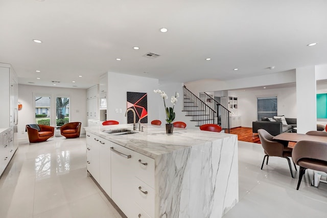 kitchen featuring visible vents, white cabinets, open floor plan, a sink, and recessed lighting