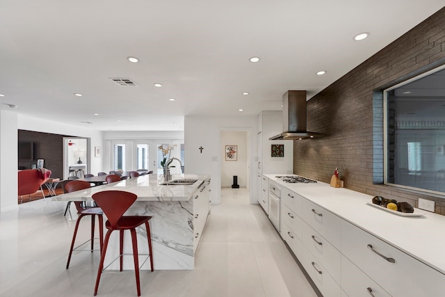 kitchen with visible vents, wall chimney exhaust hood, modern cabinets, a kitchen breakfast bar, and a sink