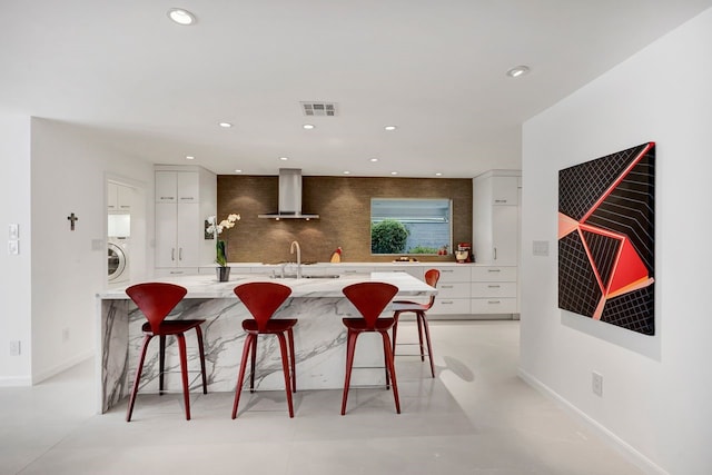 kitchen with wall chimney exhaust hood, tasteful backsplash, a breakfast bar area, and modern cabinets